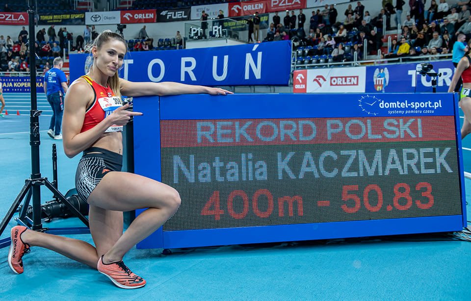 Kobieta w stroju sportowym klęka przy bilbordzie z napisem rekord Polski.