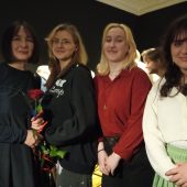 Studentki stoją obok profesor. Kobieta trzyma różę