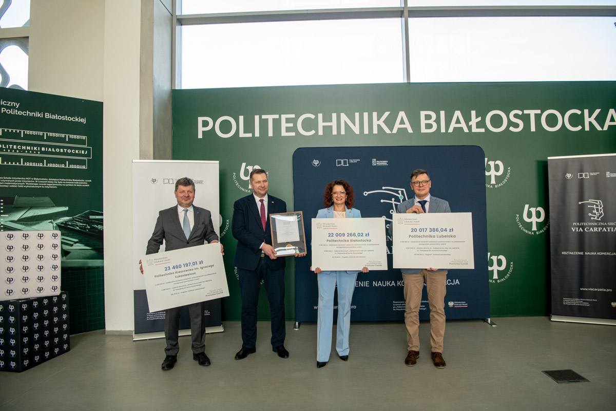 Cztery osoby pozują do zdjęcia trzymając symboliczne czeki