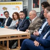 Ledzie siedzą za stołem przy mikrofonach.
