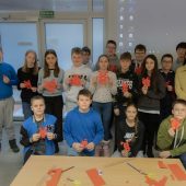 Grupa uczniów stoi w sali, prezentują wycięte z papkieru chińskie znaki królika, obok stoją wykładowcy