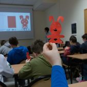 Grupa uczniów wycina z papieru chińskie znaki, jeden z nich prezentuje wycięty z czerwonego papieru znak królika