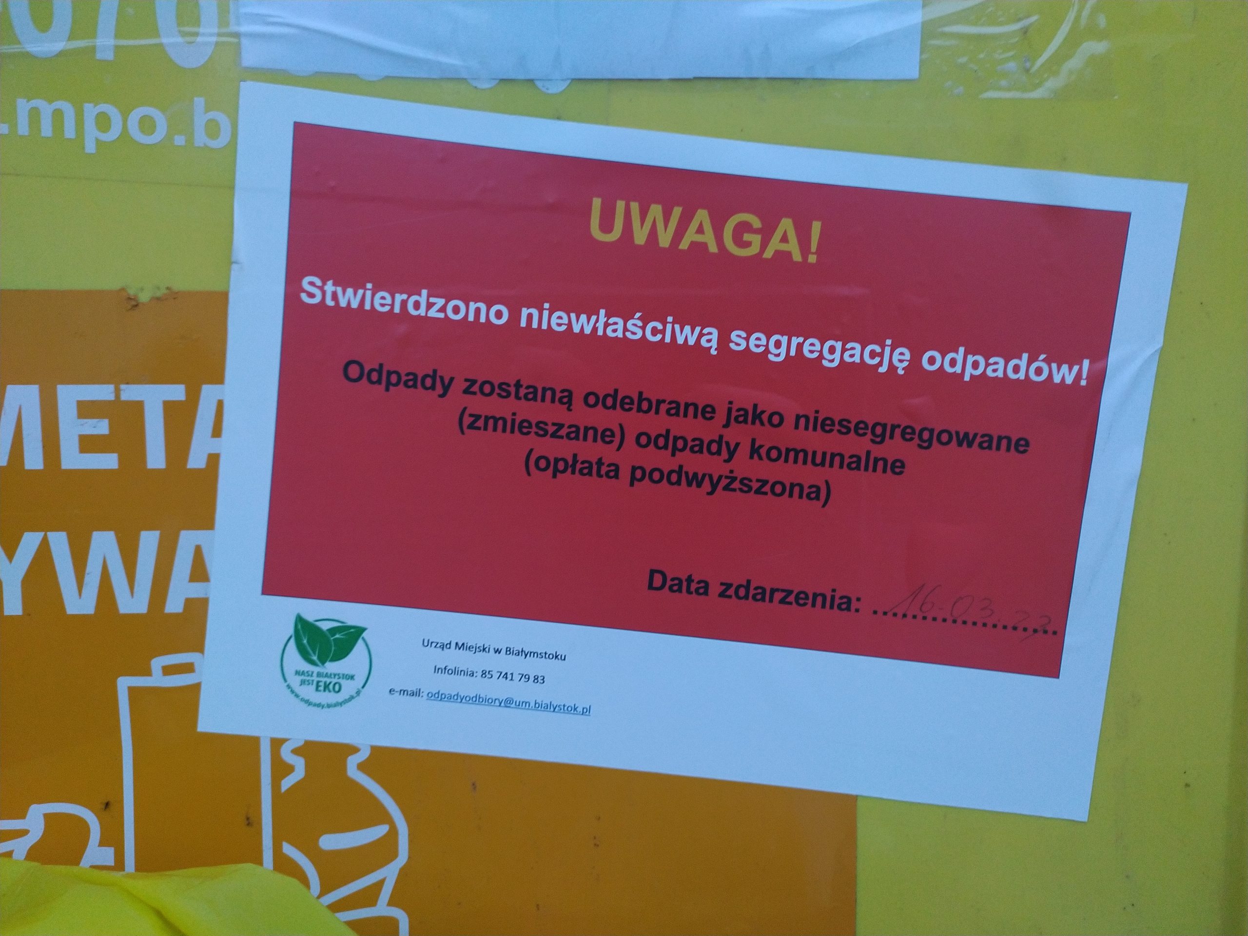 Czerwona naklejka na żółtym kontenerze na tworzywa sztuczne i metala informująca o niewłaściwej segregacji.