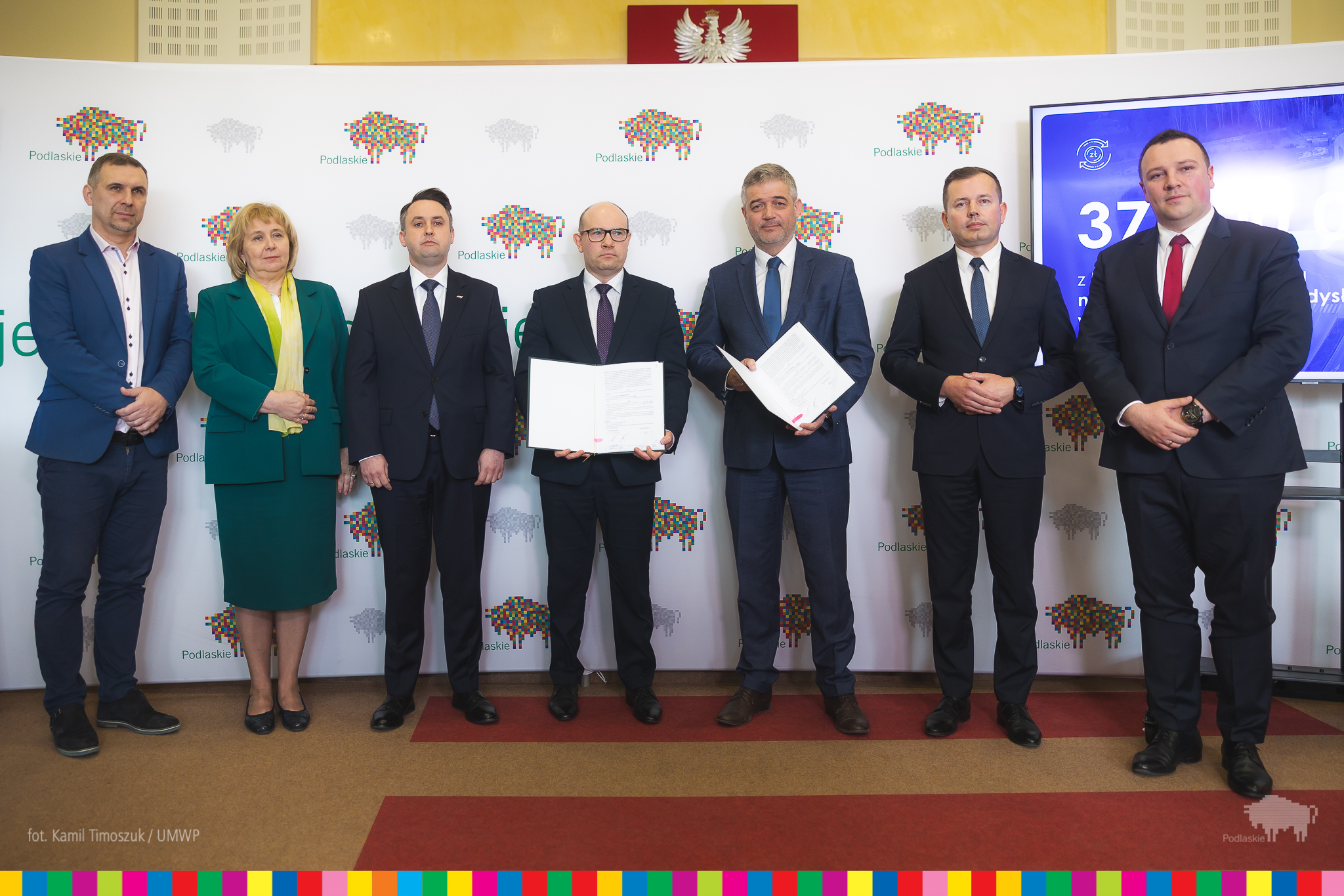 Ludzie elegancko ubrani pozują do zdjęcia, dwie osoby trzymają teczki.