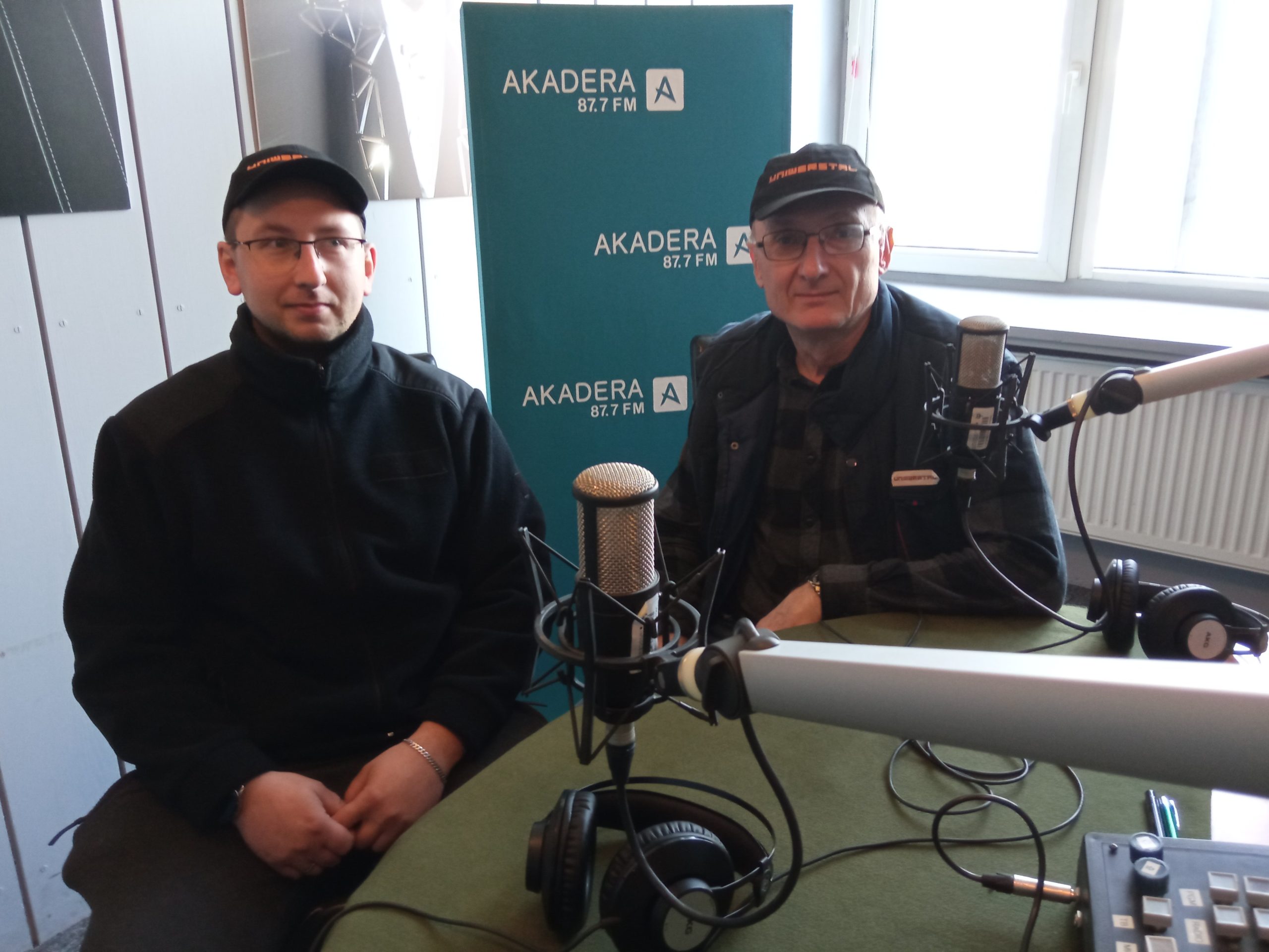 Dwóch mężczyzn siedzi przy stole w radiowym studiu