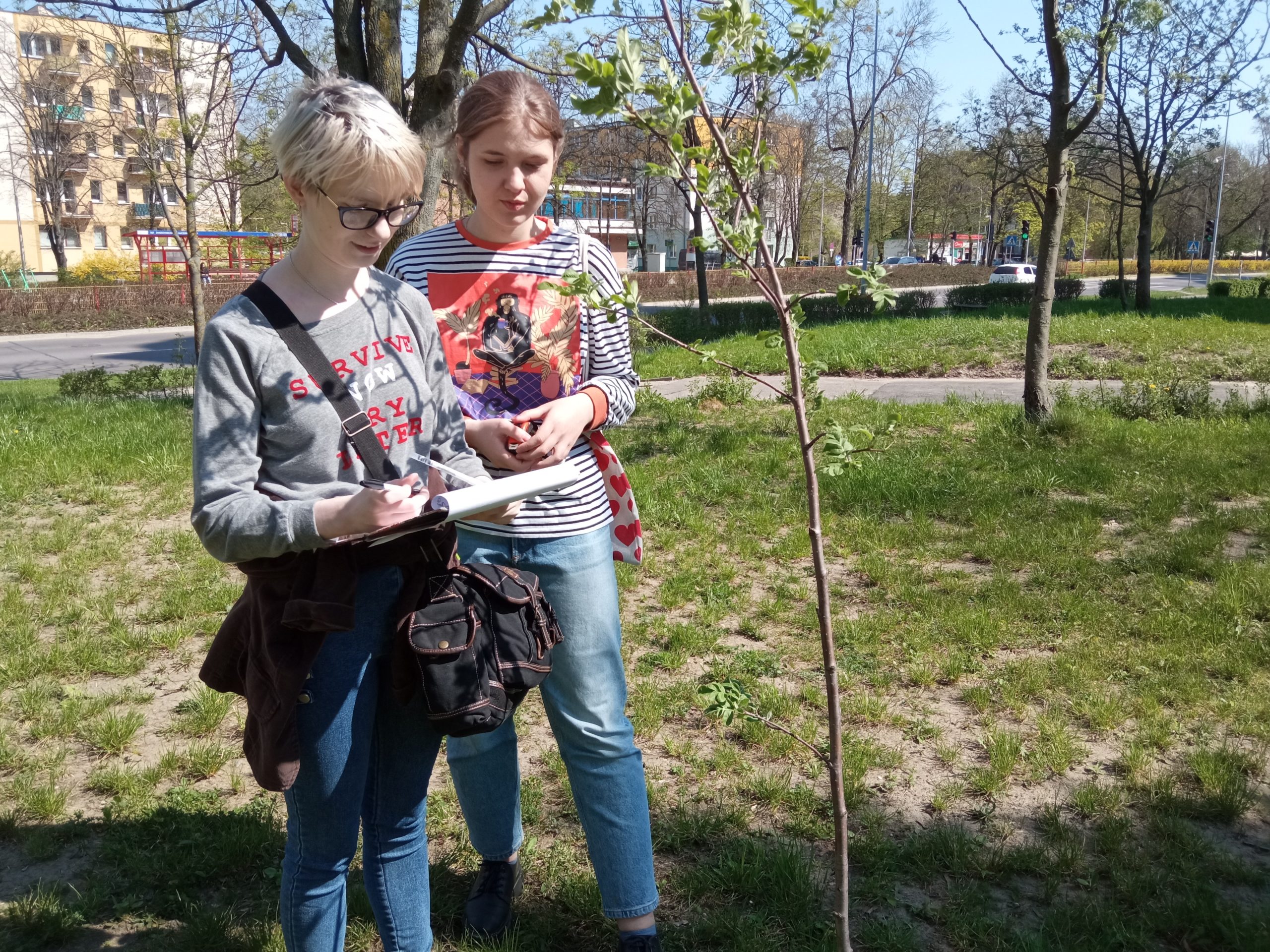 Dwie młode kobiety oglądają młode drzewo, dane zapisują w notesie