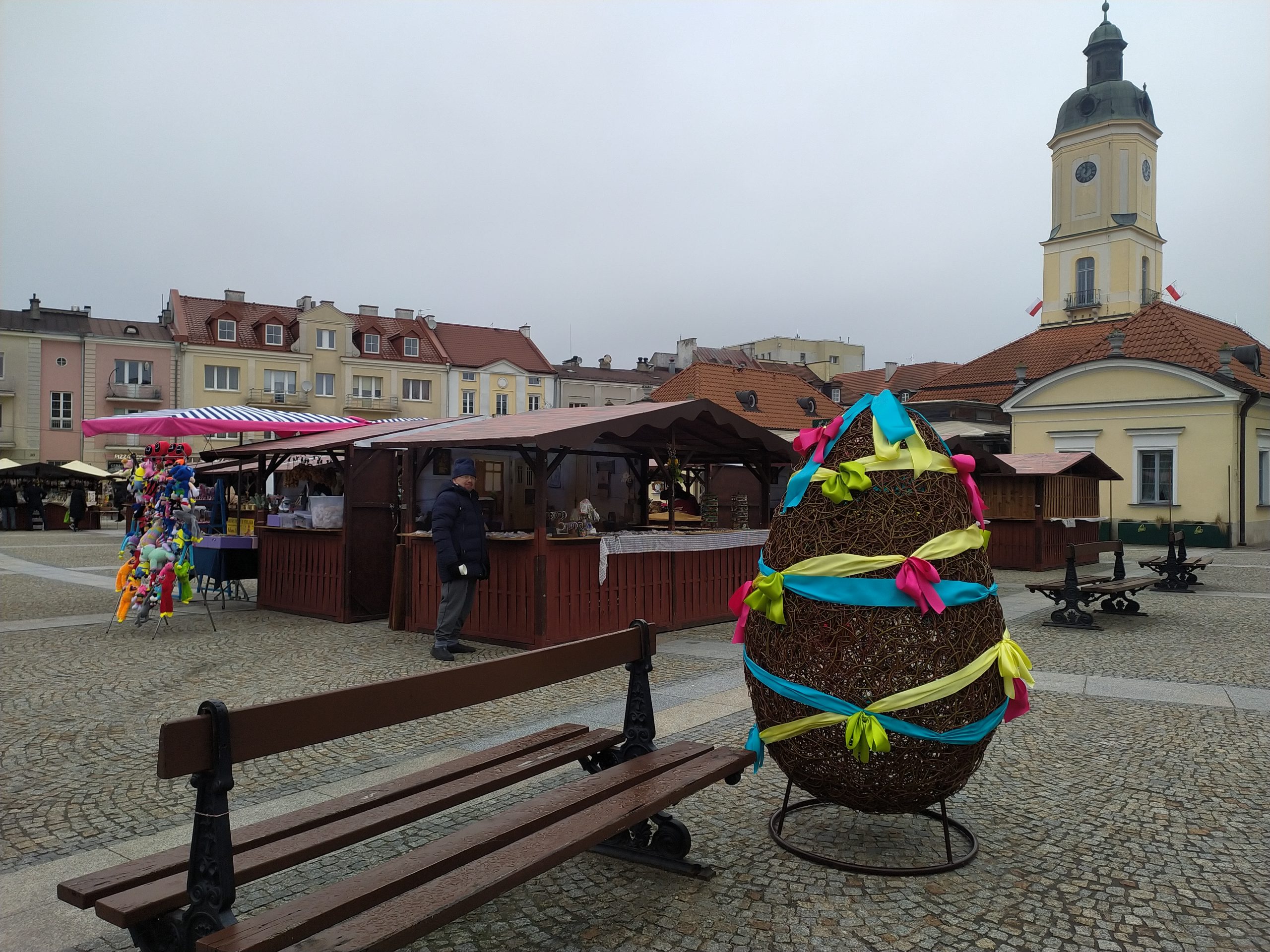 Widok na stoiska jarmarczne, w tle widać białostocki ratusz, a na pierwszym planie jest duża ozdobna pisanka.