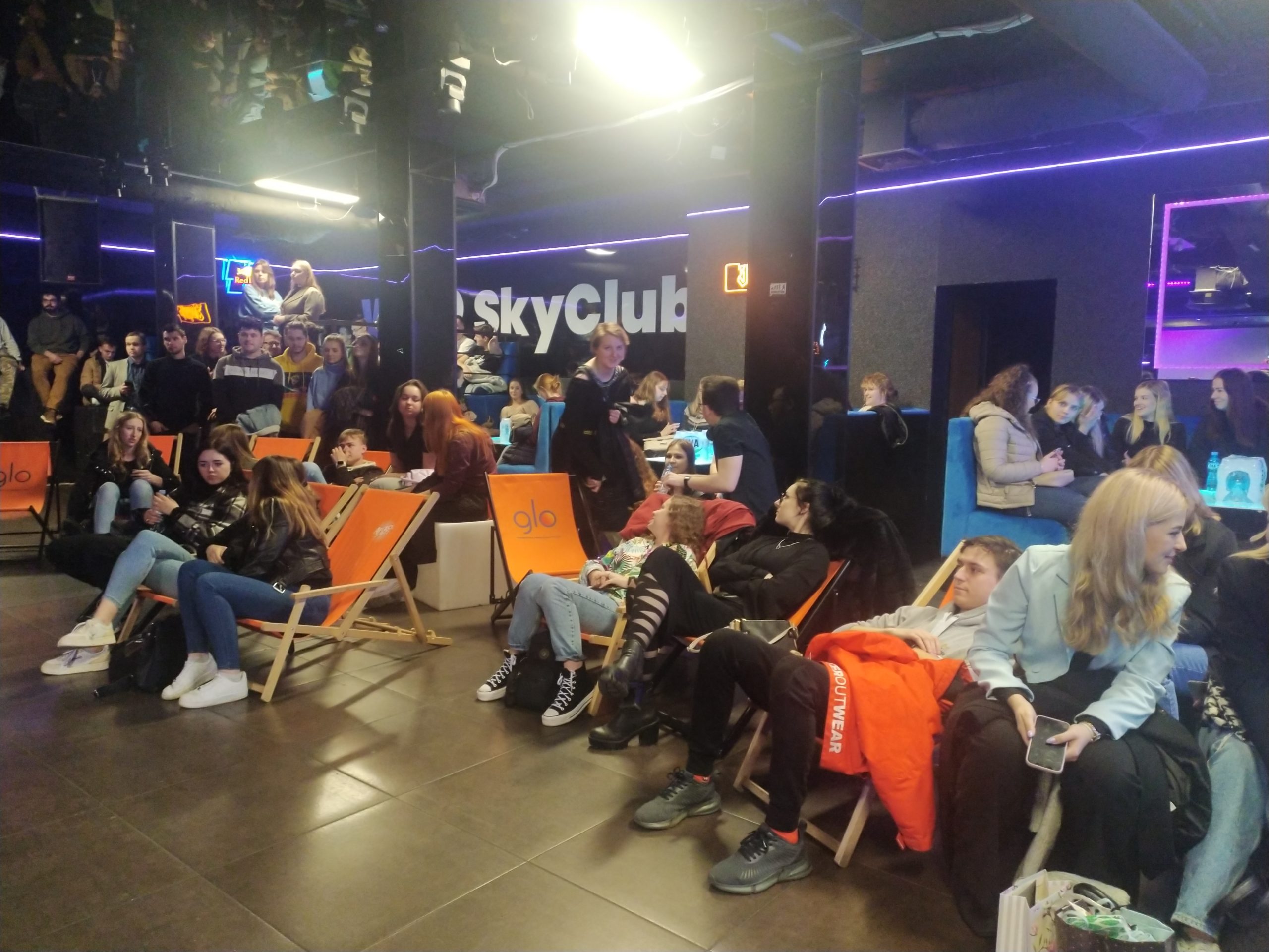 Tłum ludzi siedzi na leżakach i przy stołach w nocnym klubie,