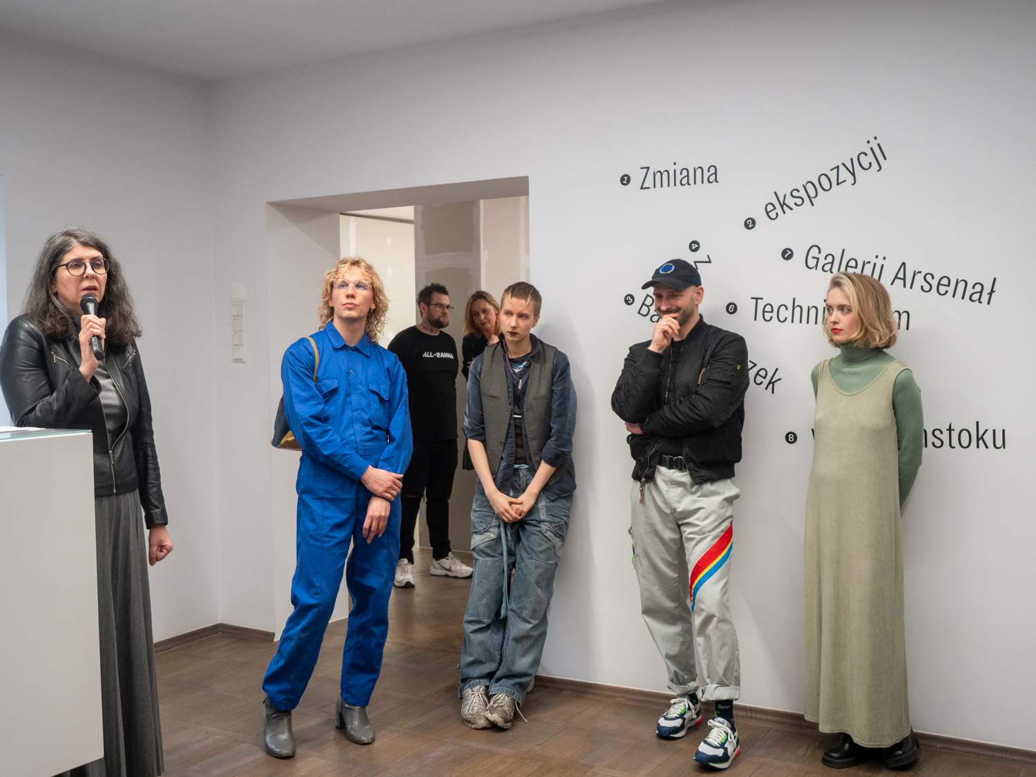 Ludzie stoją pod ścianą w trakcie wernisażu wystawy
