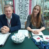 Mężczyzna i kobieta siedzą za stołem, na stole leżą identyfikatory oraz dokumenty