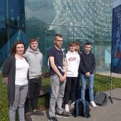 Grupa uczniów wraz z nauczycielką stoją przed wejsciem do budynku uczelni