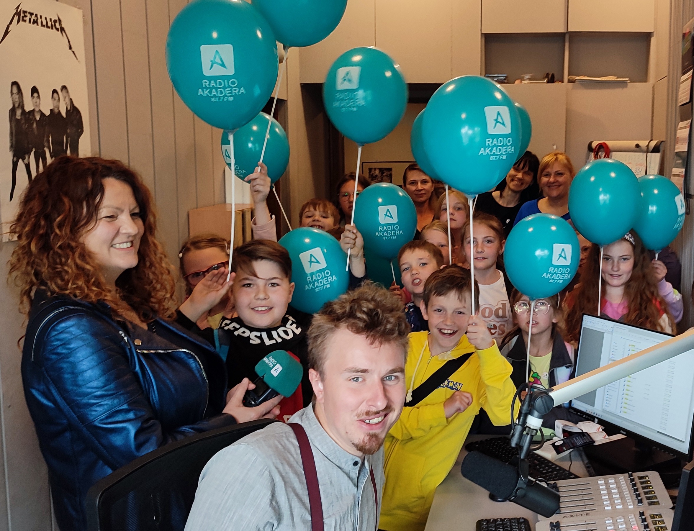 Dzieci trzymają niebieskie balony stojąc w studio radiowym.