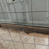 Szary budynke ogrodzony siatką, odsłonięte fundamenty