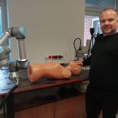 Mężczyzna stoi przy fantomie. Obok na stole umieszczony prototyp robota