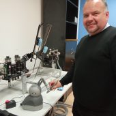 Mężczyzyna stoi rzy stole, na którym umieszczony jest robot; trzyma strerownik