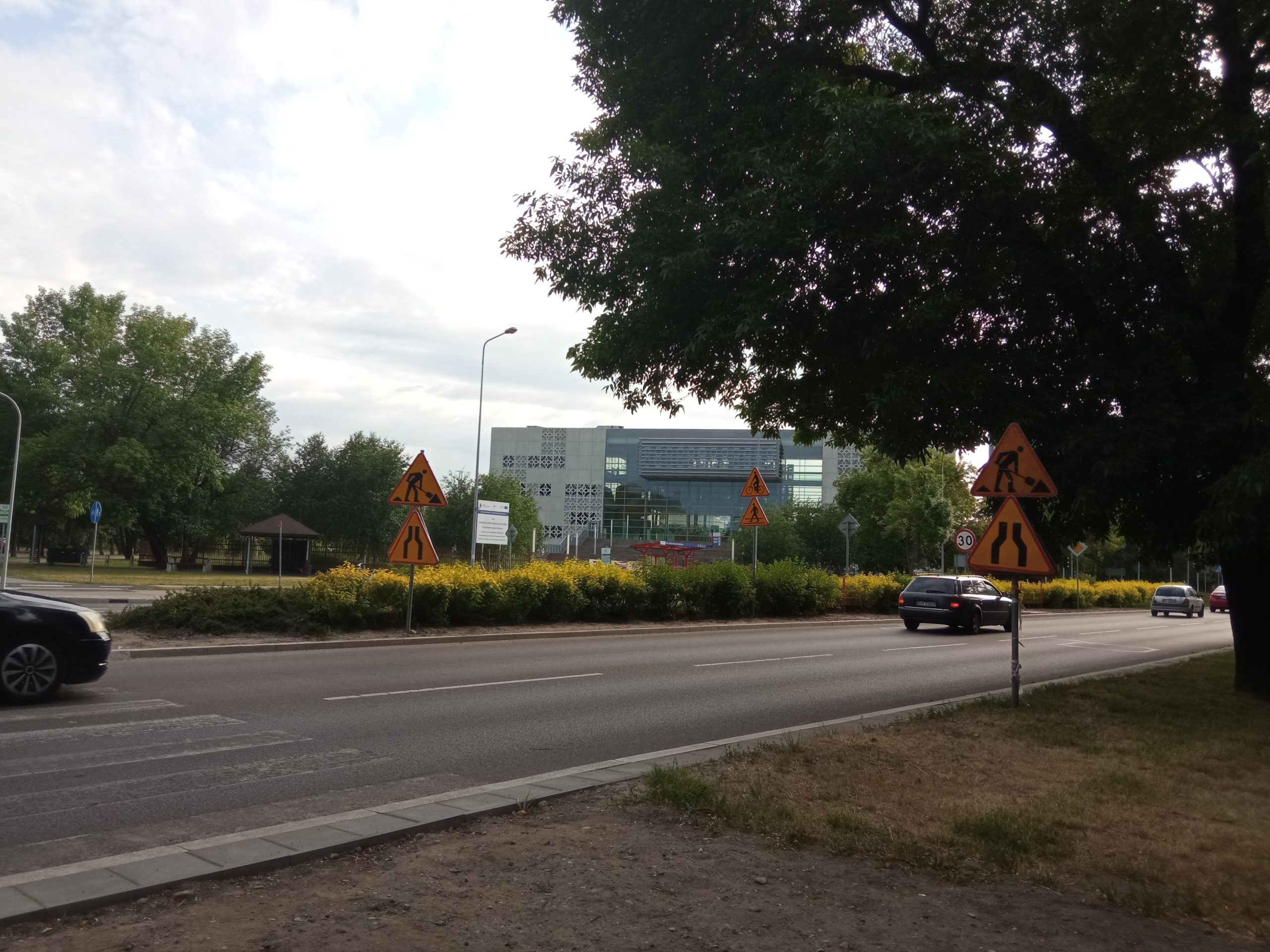 Ulicą jada samochody, na poboczach znaki drogowe informujące o robotach drogowych
