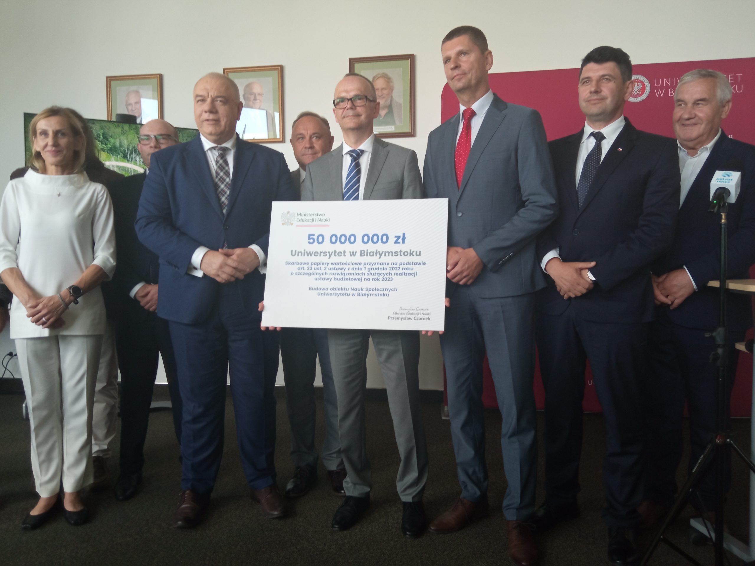 Panowi w garniturach prezentują symboliczny czek z napisem 50 mln zł