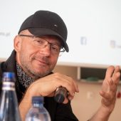 Mężczyzna macha do obiektywu.