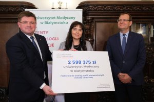 Trzy osoby pozują do zdjęcia z symbolicznym czekiem w rękach.