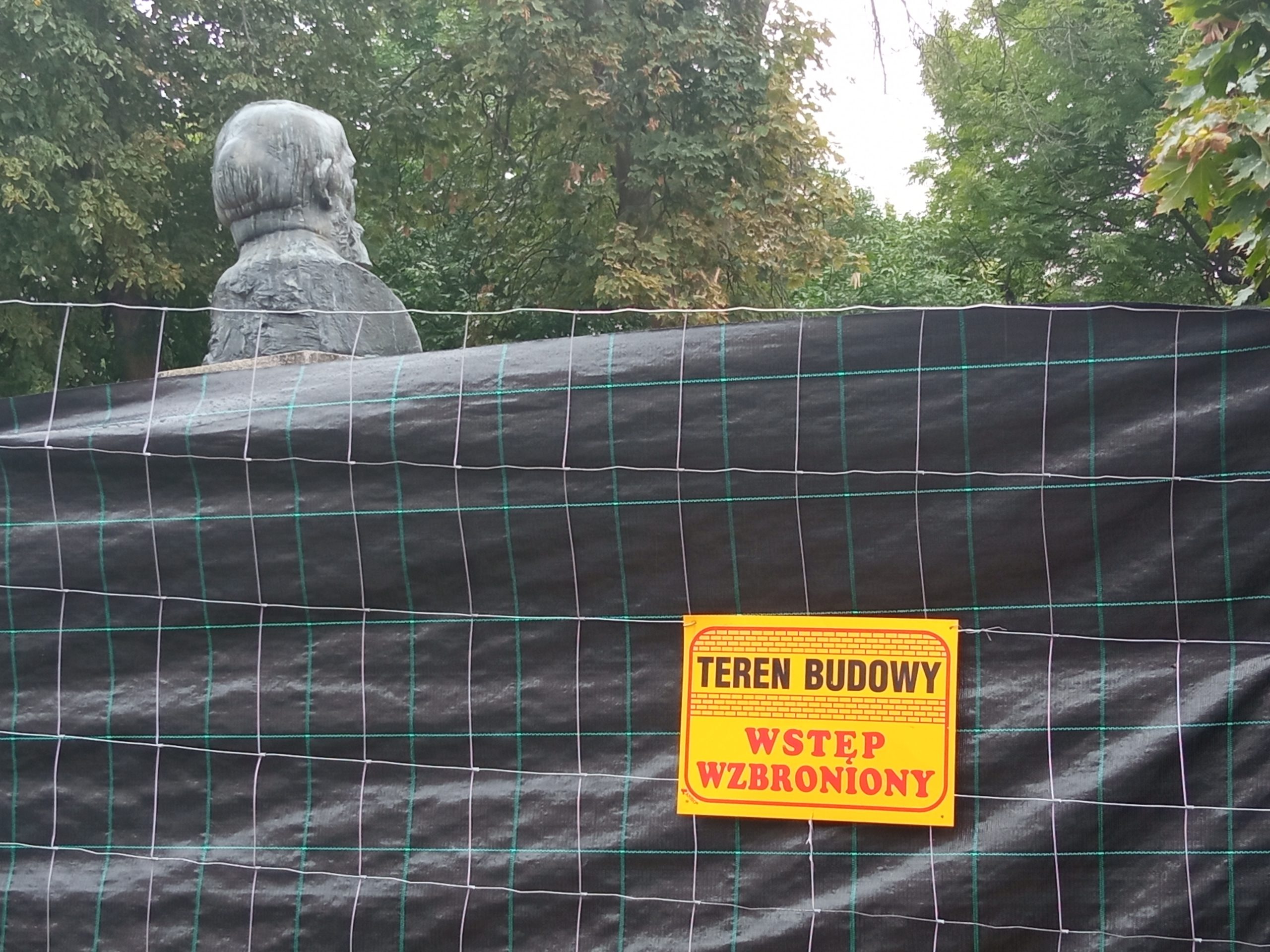 Ogrodzony siatką i folią skwer im. P. Adamowicza. Widać tyłem pomnik Zamenhofa