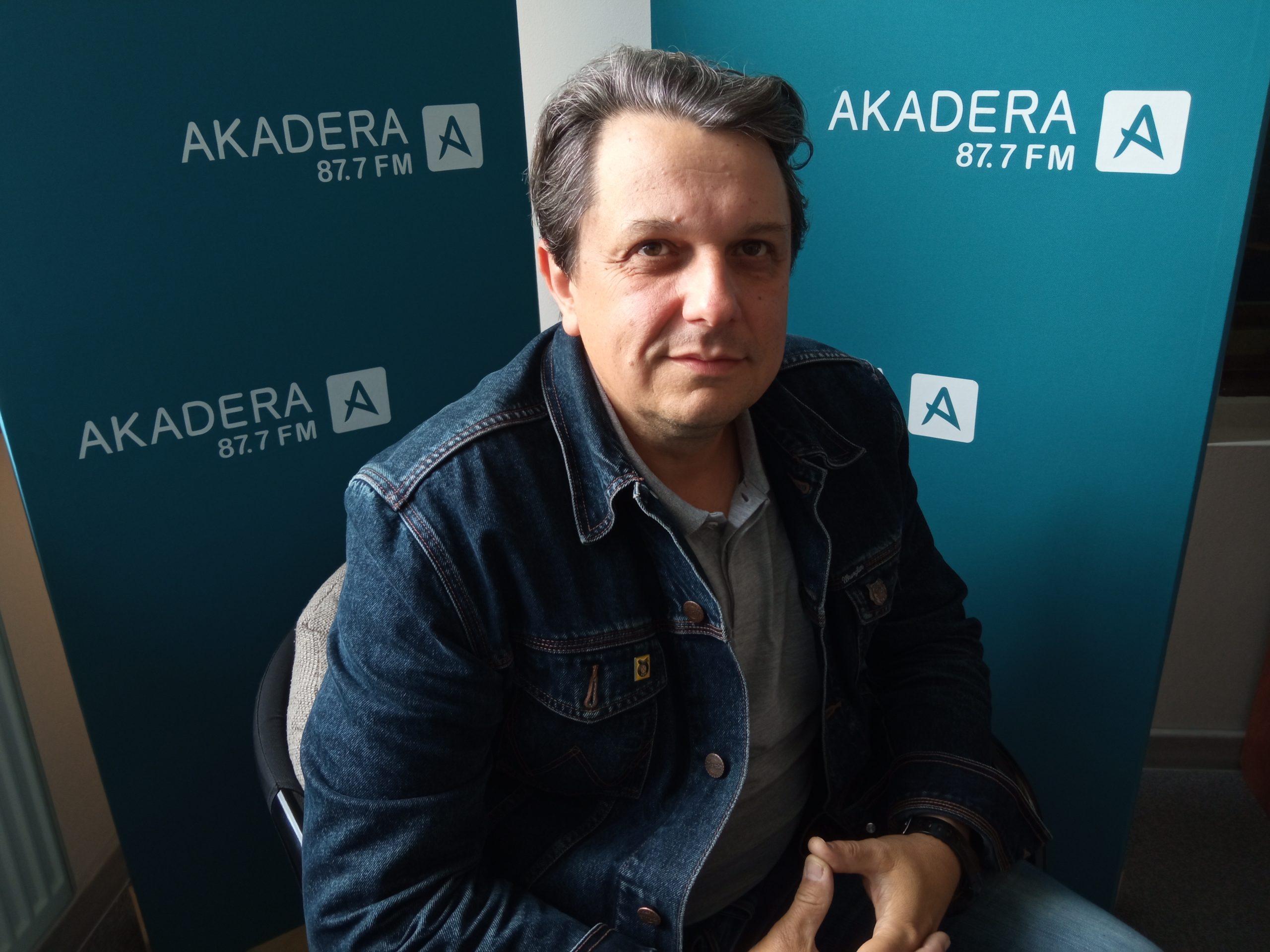Mężczyzna siedzi na fotelu, w tle logo radia
