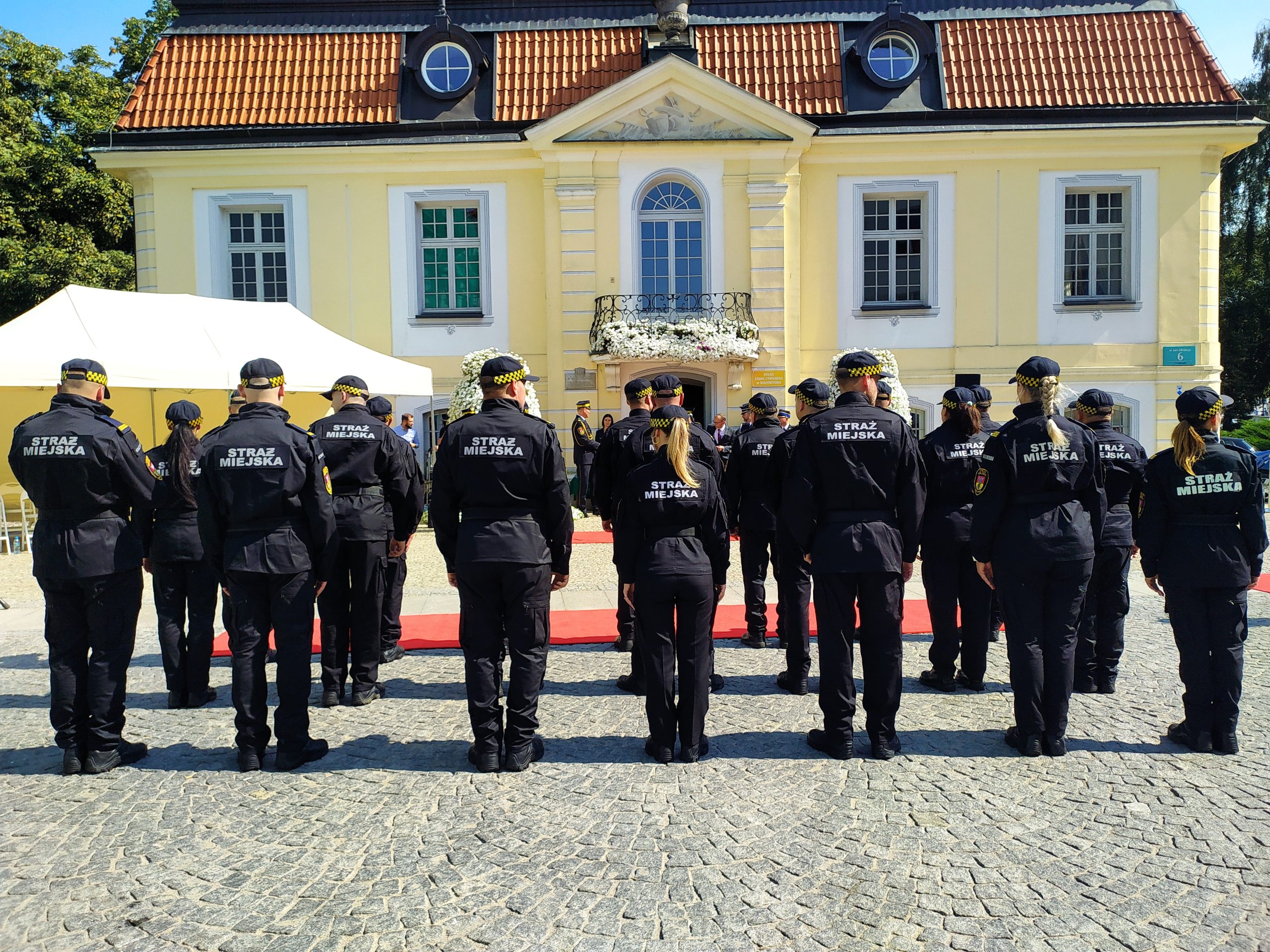 Kilkudziesięciu strażników miejskich stoi na podwórku.,