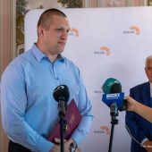 Przed mężczyzną stoją mikrofony.