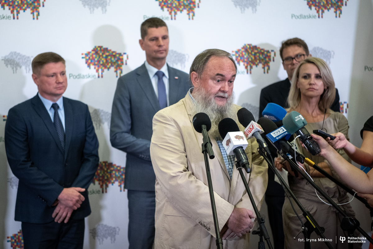 Mężczyzna z brodą w garniturze mówi do mikrofonów dziennikarzy