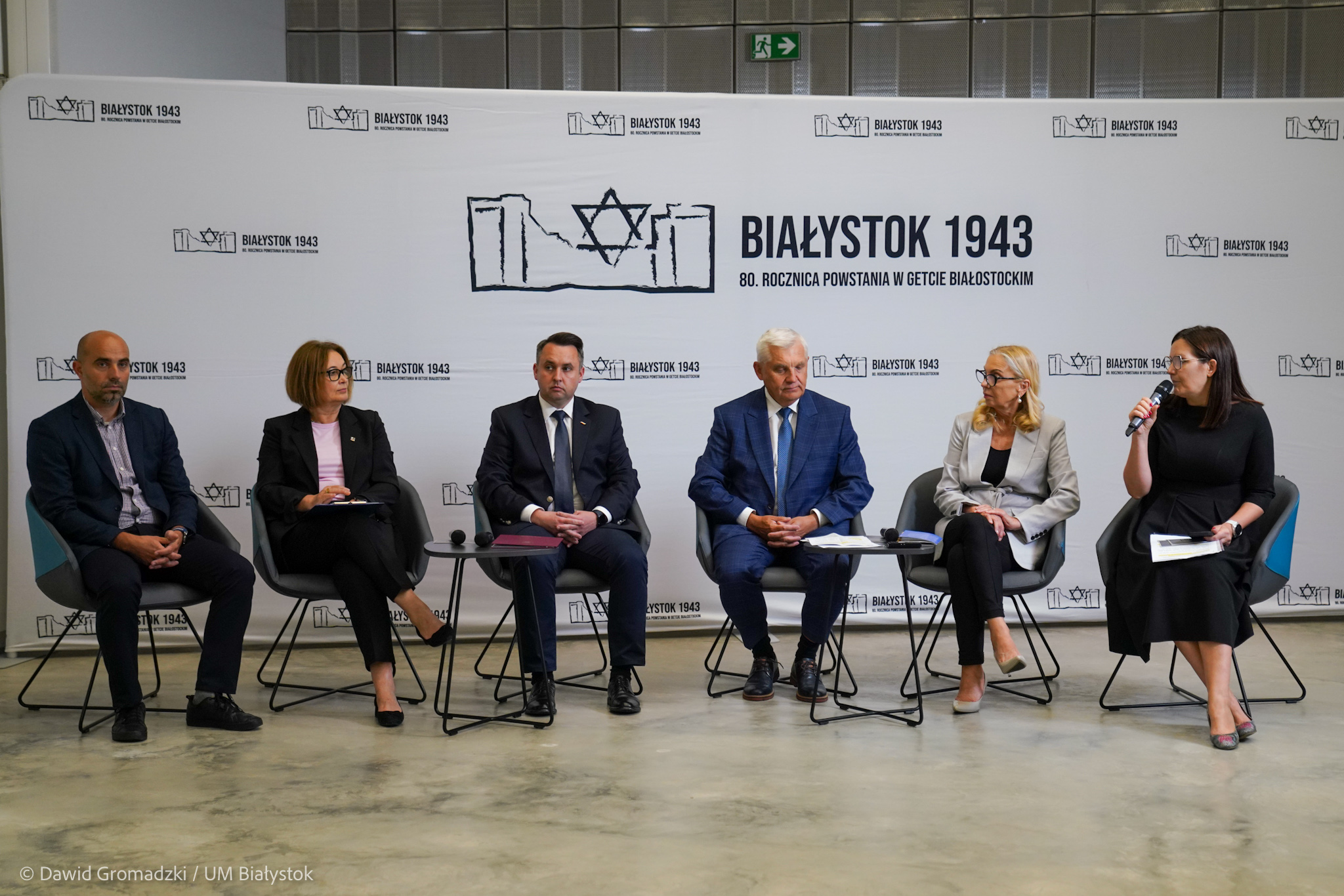 Sześć osób siedzi na krzesłach przed ścianką promującą wydarzenia związane z 80. rocznica Powstania w Getcie Białostockim