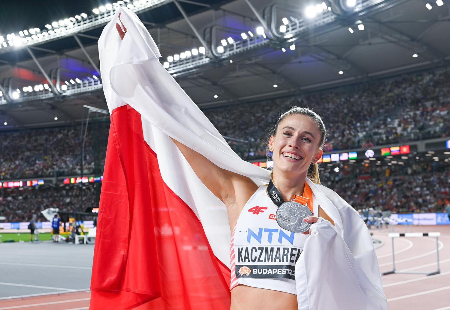 Kobieta w sportowym stroju cieszy się trzymając flagę Polski.