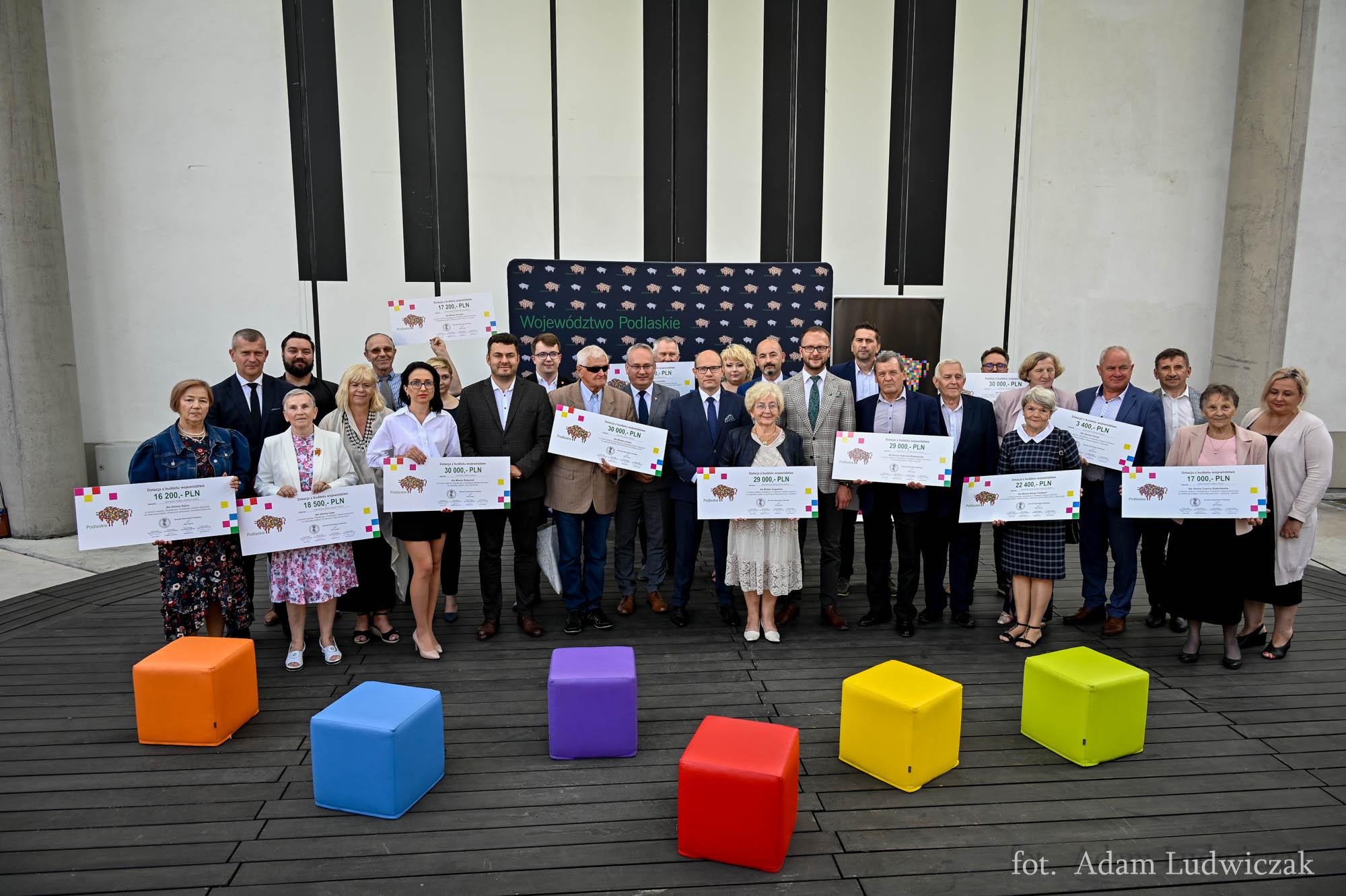 Grupa osób pozuje do zdjęcia, niektórzy trzymają symbloiczne czeki