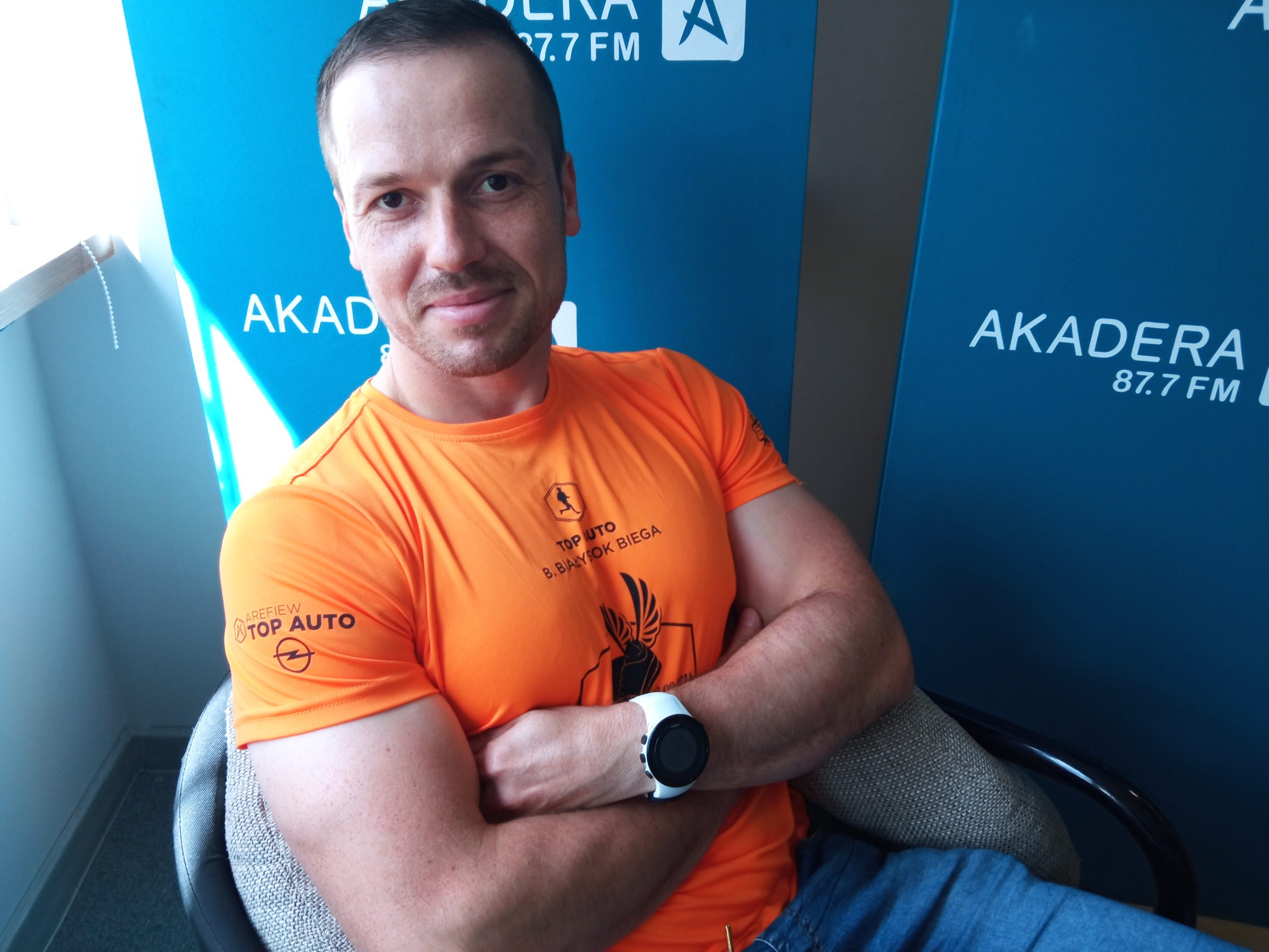 Mężczyzna w sportowej koszulce siedzi na fotelu, w tle logo radia