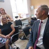 NA fryzjerskich krzesłach siedzą kobieta i mężczyzna, młoda dziewczyna układa włosy kobiety