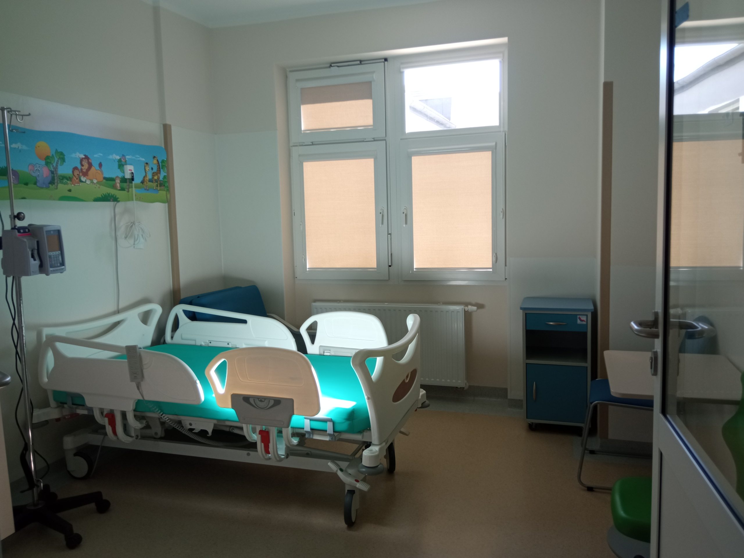 djecie przedstawia izolatkę na oddziale onkologicznym dla dzieci. To łóżko dl dziecka, obok fotel dla rodzica, panel na ścianie w kolorowe zwierzaki