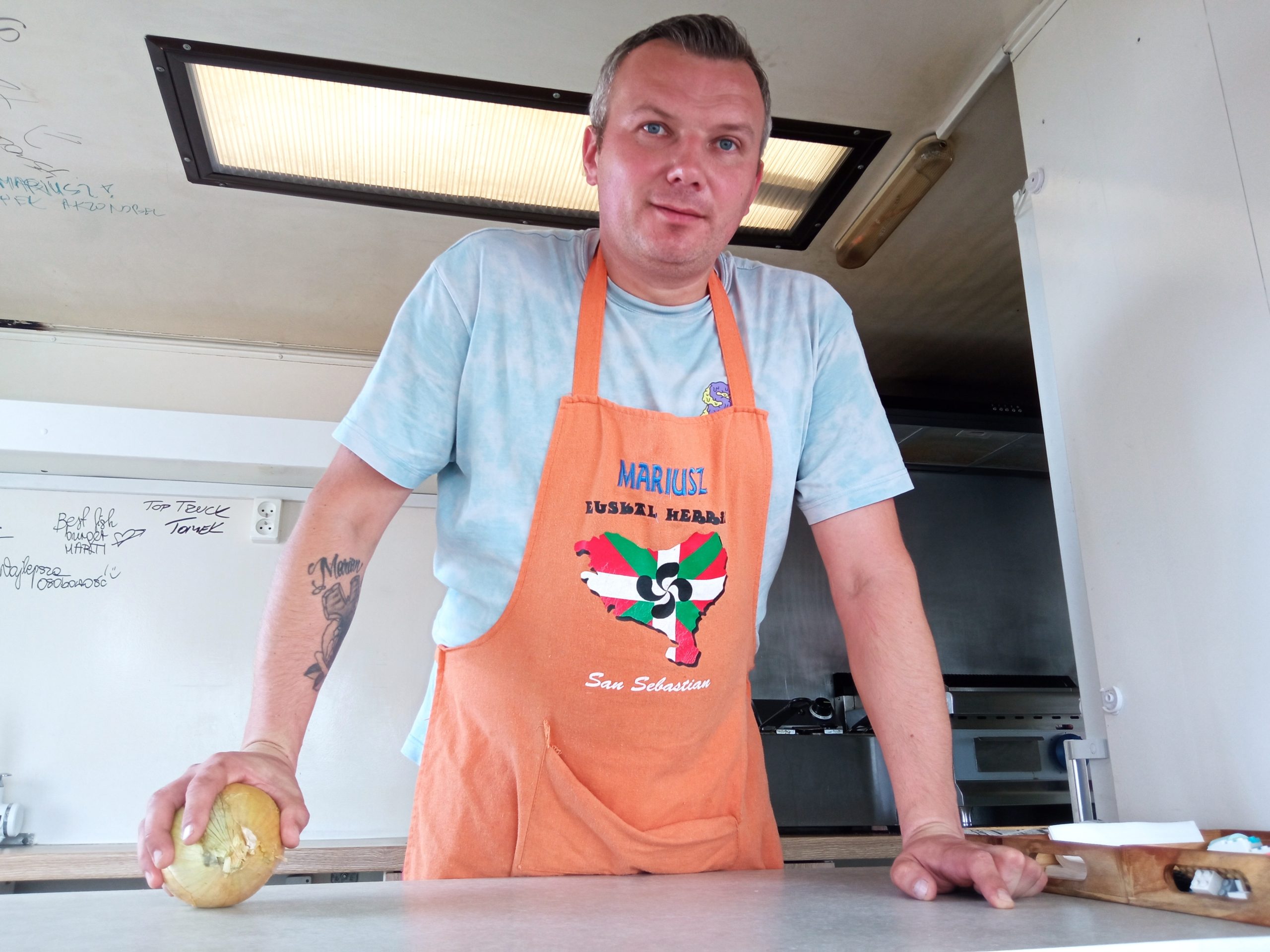Mężczyzna w kuchennym fartuchu stoi w otwartym oknie food trucka