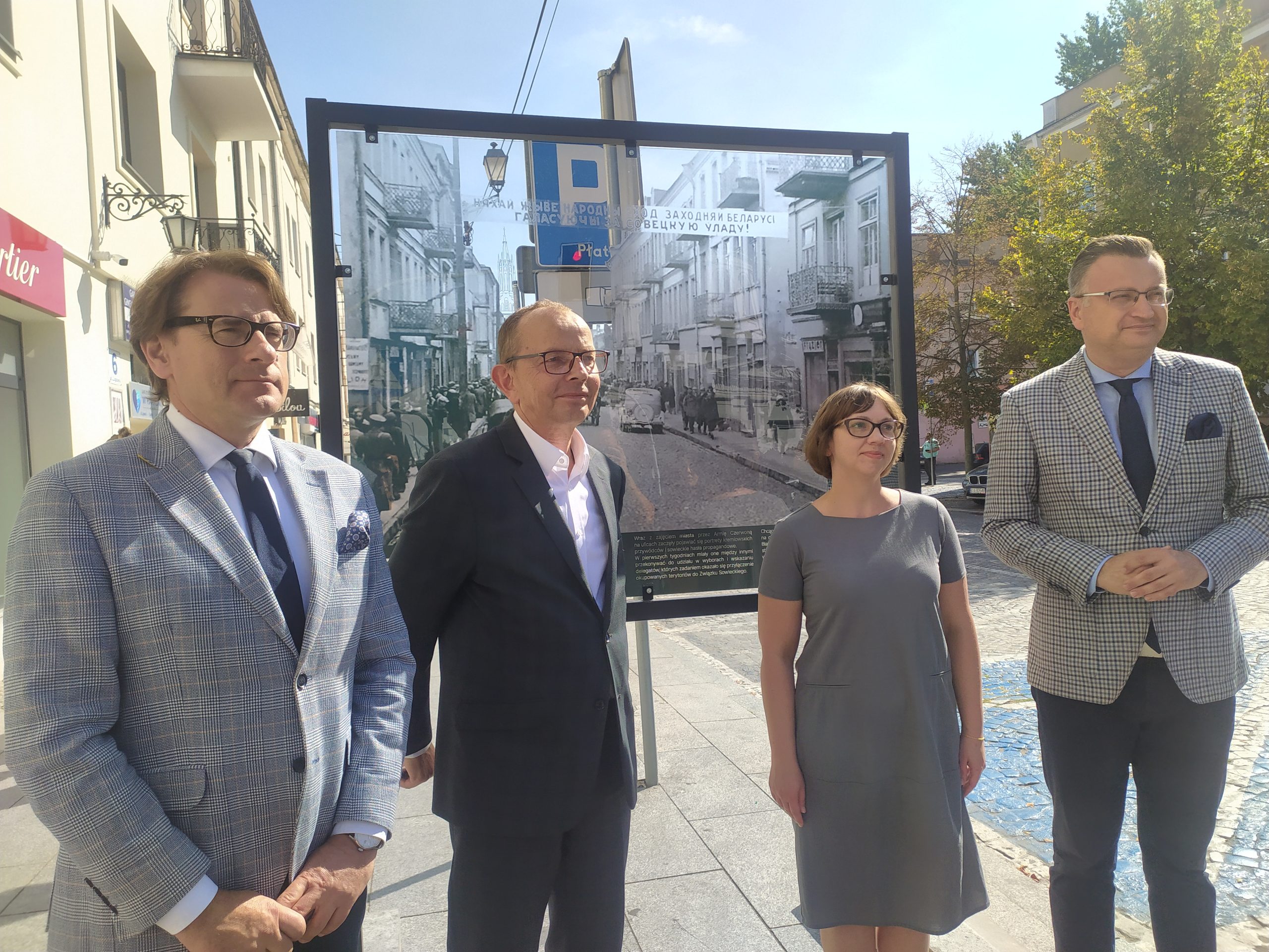 Cztery osoby pozują do zdjęcia na tle zdjęcia w centrum miasta.