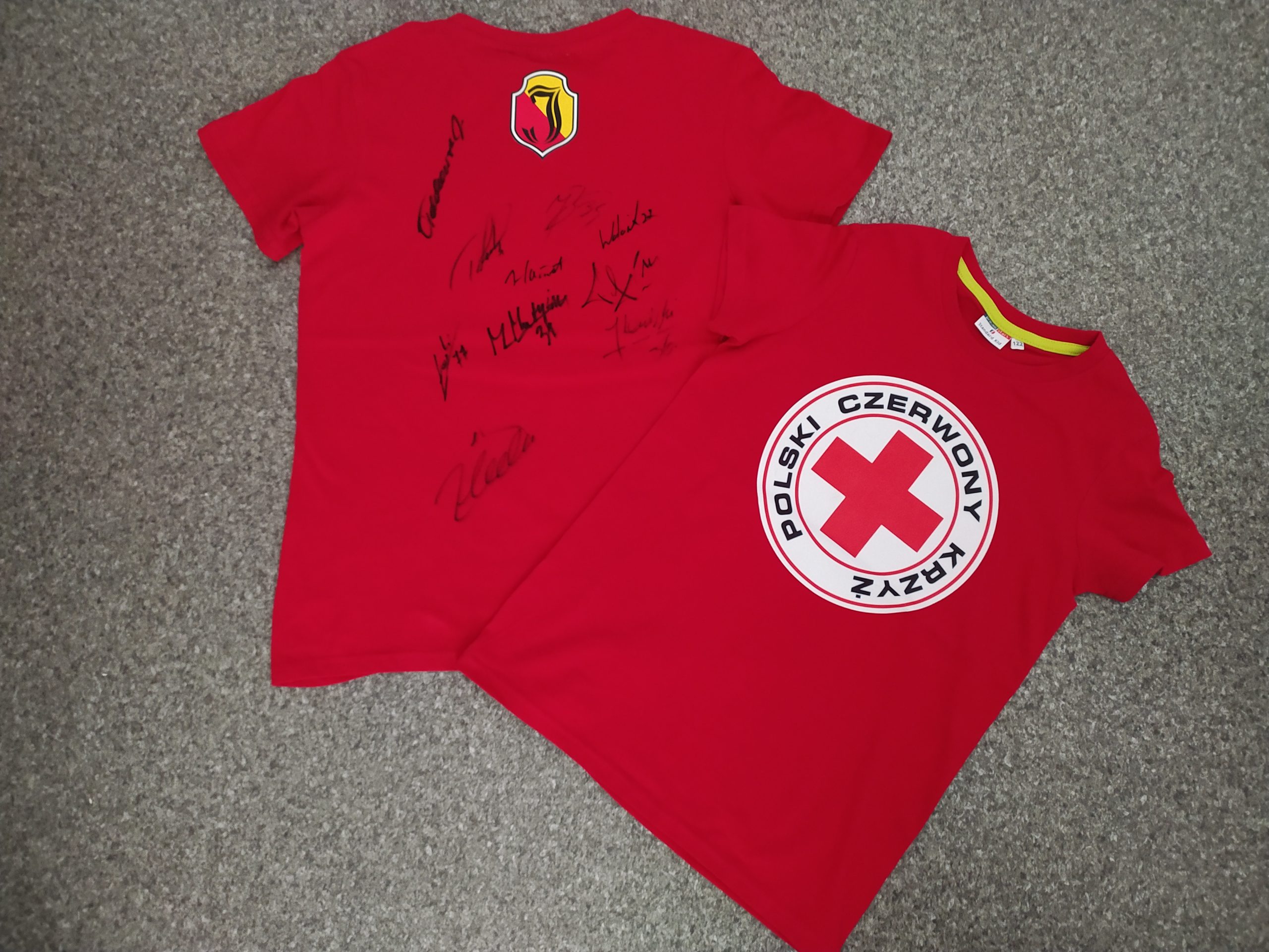Dwie czerwone koszulki, na jednej logo PCK, a na drugiej autografy.