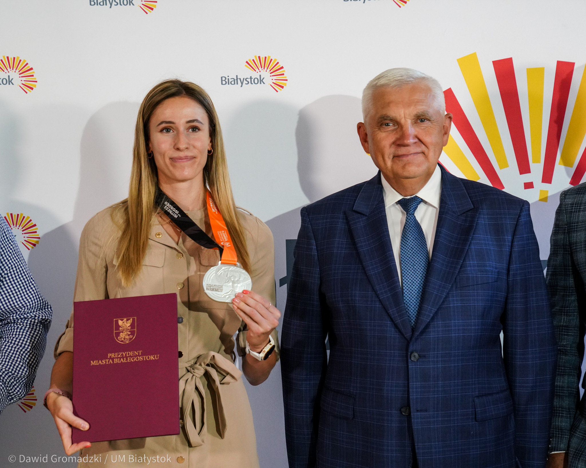 Kobiet prezentuje srebrny medal, obok stoi mężczyzna w garniturze