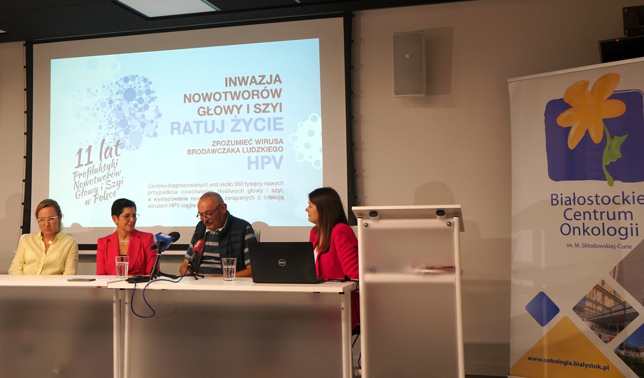 Cztery osoby siedzą przy stole, za nimi prezentacja multimedialna.