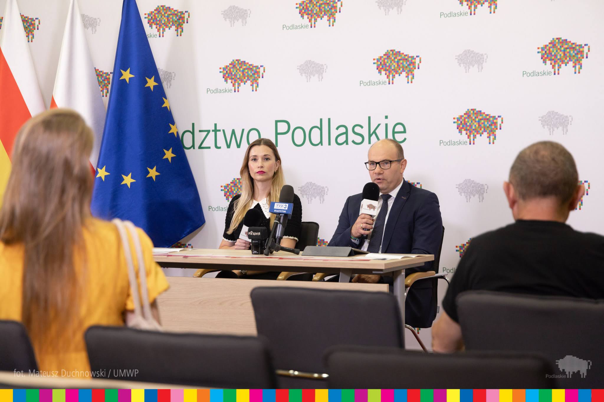 Kobieta i mężczyzna siedzą przy stole przed mikrofonami.