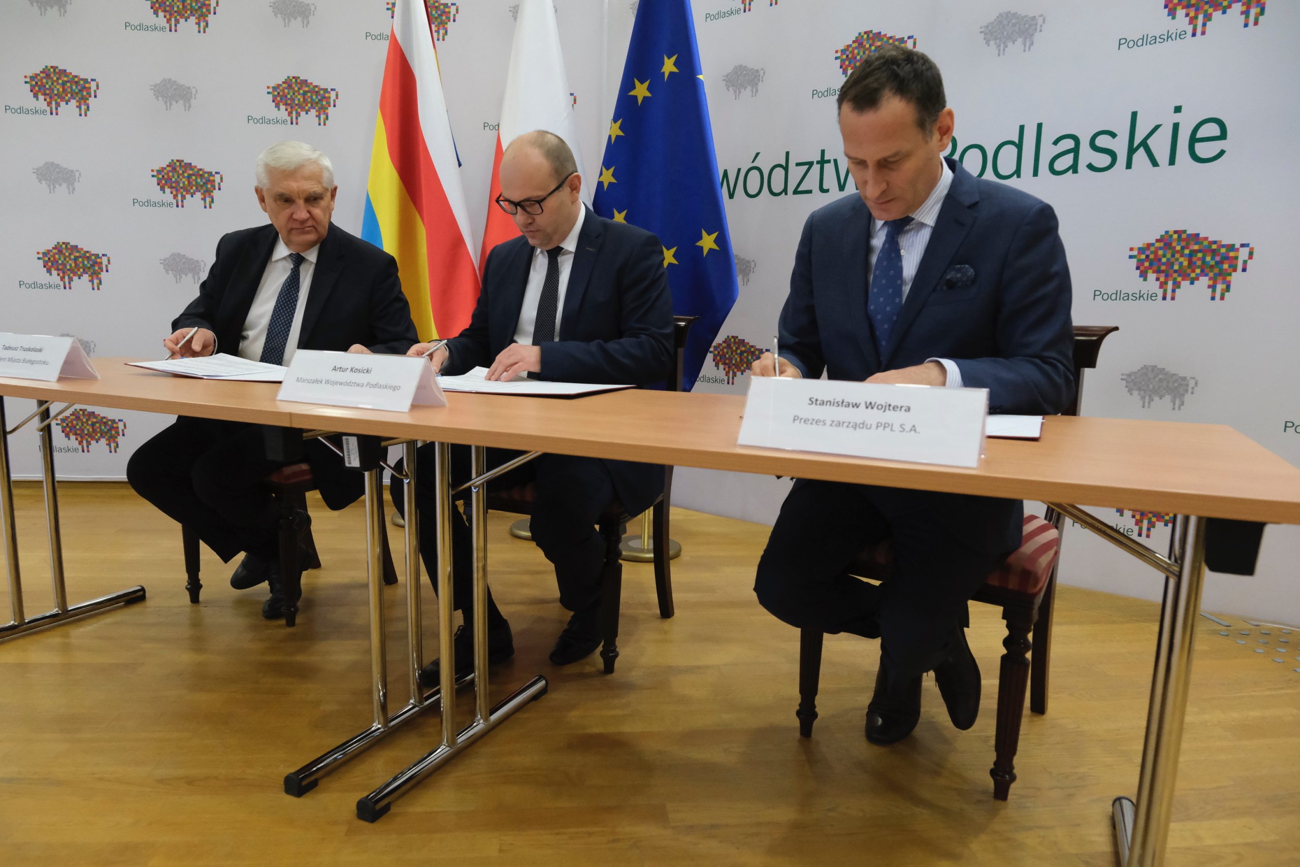 Trzech mężczyzn podpisuje dokumenty przy stole.