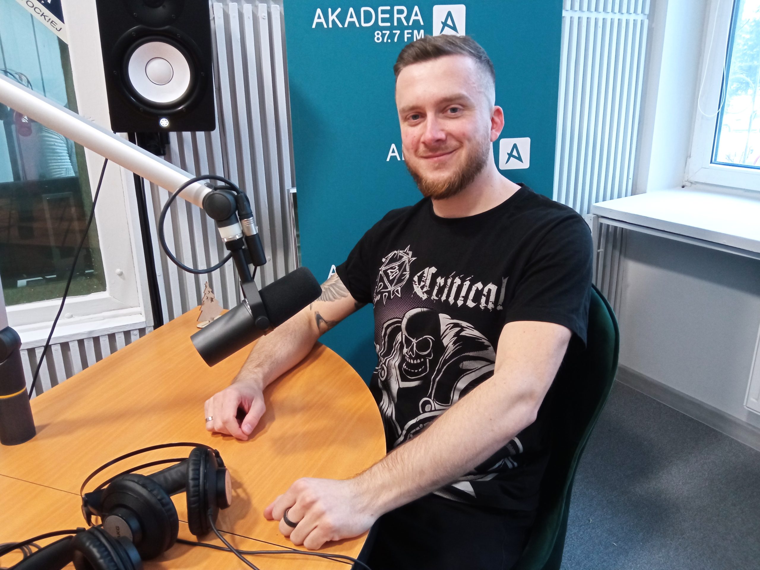 Młody mężczyzna siedzi przy stole przed mikrofonem w radiowym studiu