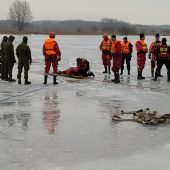 Strażacy stoją na zamarzniętym jeziorze i wyciągają jedną osobę z wody,
