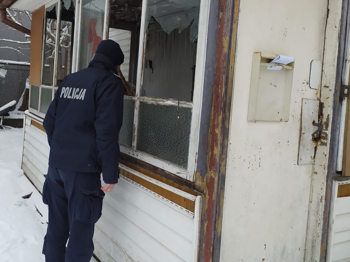Policjant zagląda do budynku przez wybitą szybę w oknie