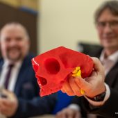Dwóch mężczyzn trzyma czaszkę wydrukowaną na drukarce 3D