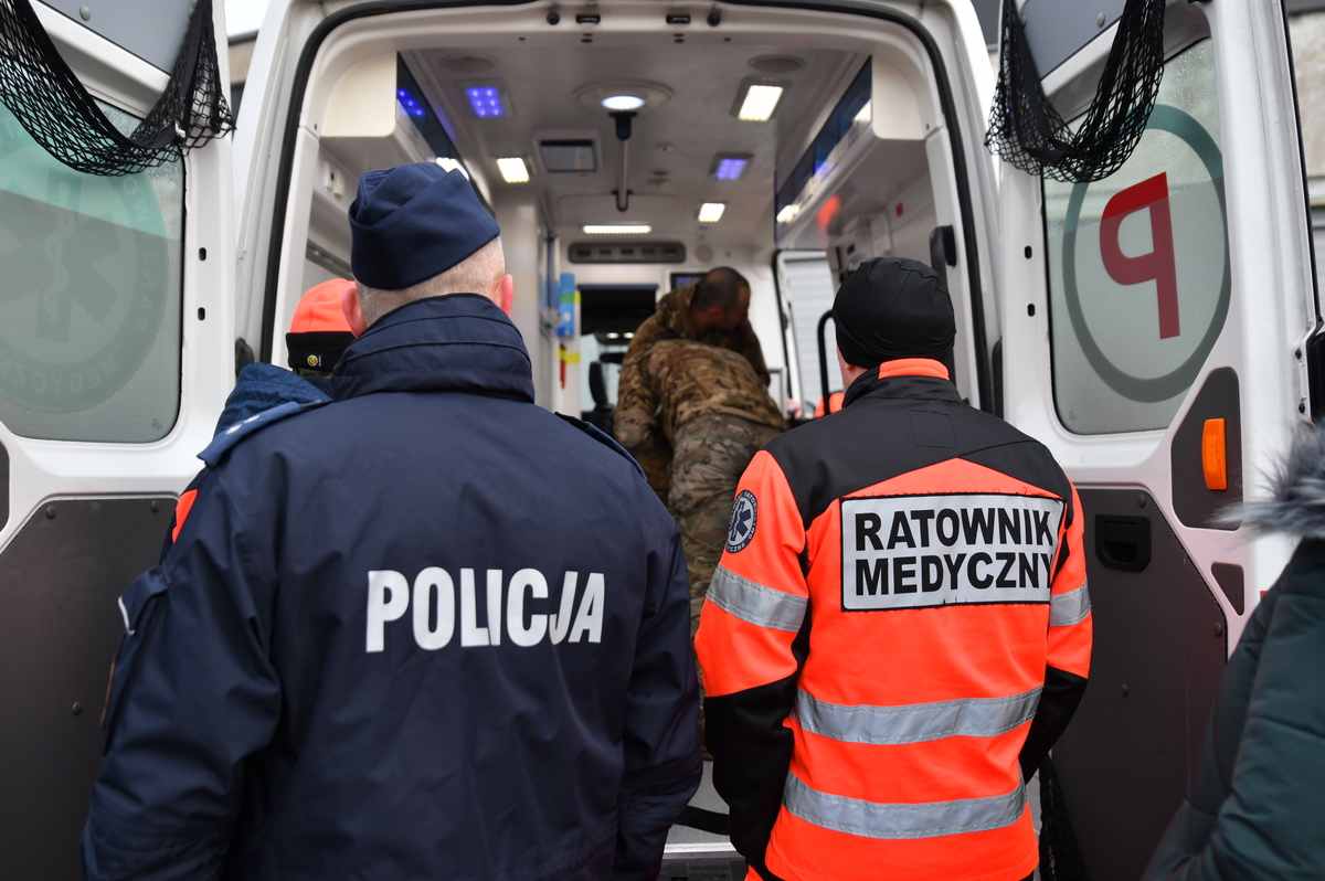 Policjant i ratownik medyczny przed otwartymi drzwiami karetki pogotowia.