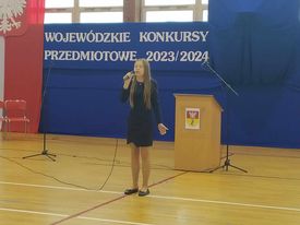 Dziewczyna śpiewa do mikrofonu w sali gimnastycznej.