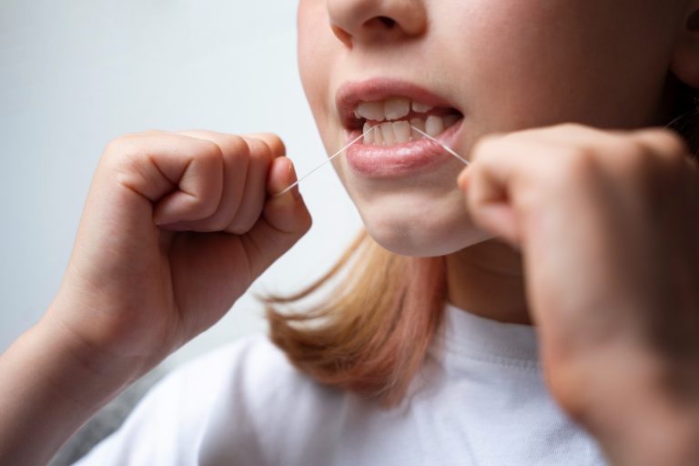 dziewczynka czyści zęby nicią dentystyczną