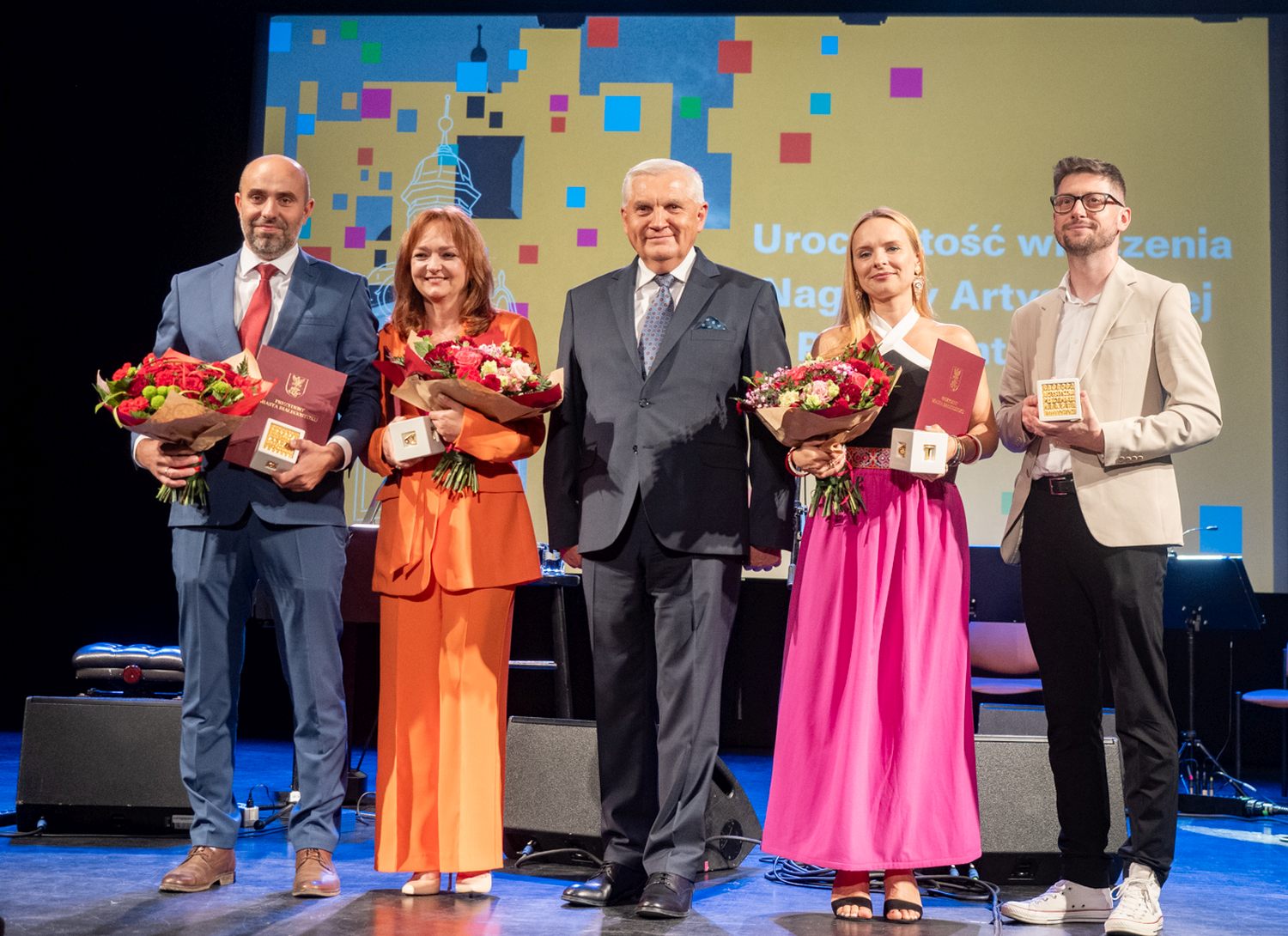 % elegancko ubranych osób pozuje do zdjęcia stojąc na scenie.