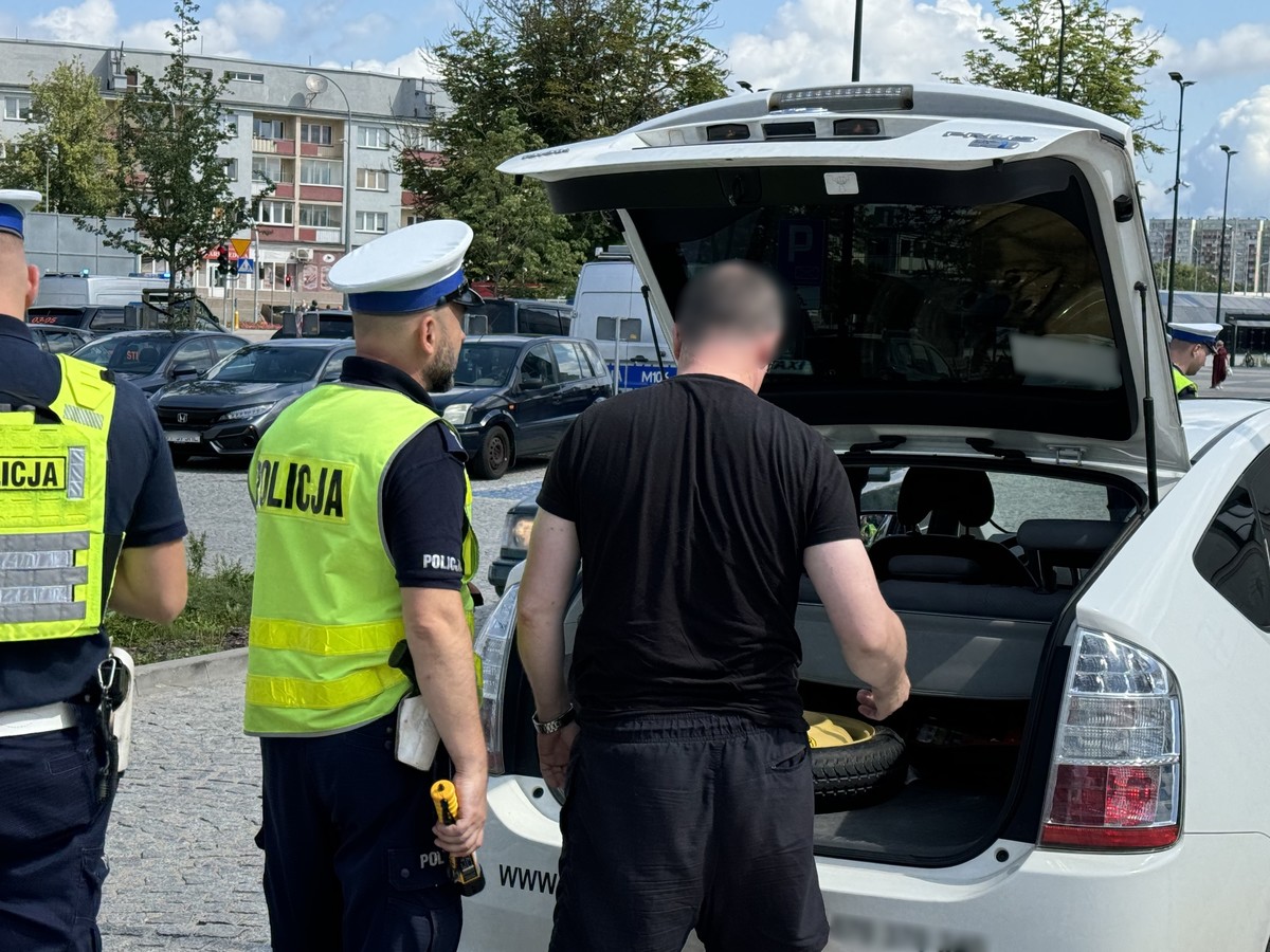 Policjant i kierowca stoją przed bagażnikiem auta